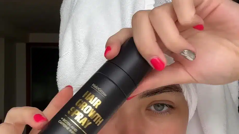 Anwenderin mit Handtuch hÀlt die HaloGrow Haarspray Flasche nach dem Duschen